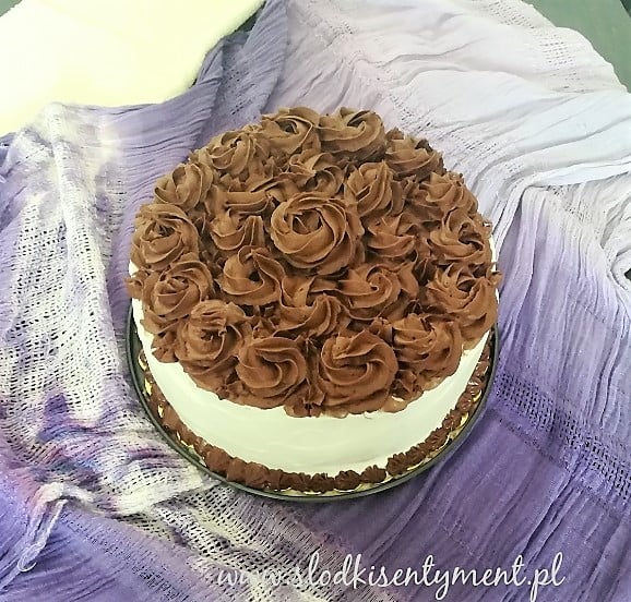 biały tort z czekoladowymi kwiatami na fioletowym tle